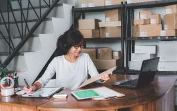 Woman in an office sitting at desk looking and smiling at clipboard.