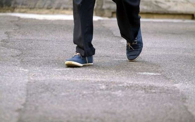 Person in black pants and blue shoes jaywalking across street