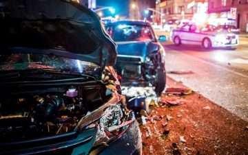 Two black cars with damage, police in the background after multi-car accident.