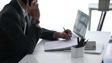 Man at desk with pen and paper and computer at desk. We explain 5 common mistakes to avoid during your personal injury case.
