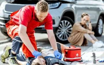Male paramedic assisting unconsciousness man, woman in background leaning on car with concerned look. How to prove fault in a pedestrian accident In New York.