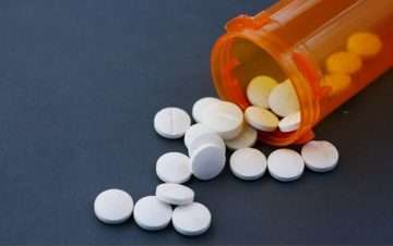 Orange pill bottle with white pills spilling. Sign of what can happen during a dangerous drug injury.