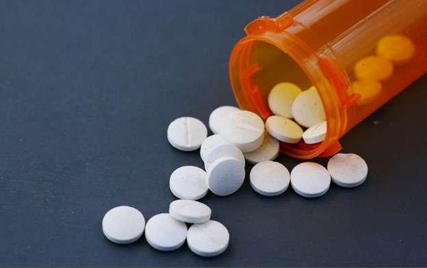 Orange pill bottle with white pills spilling. Sign of what can happen during a dangerous drug injury.