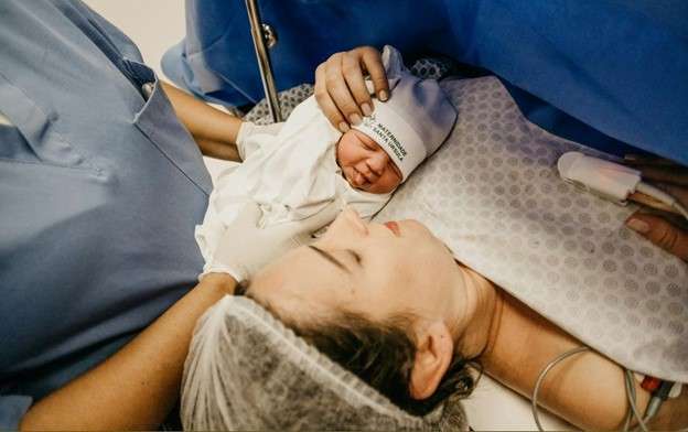 Newborn baby in delivery room with mother lying down. Birth injuries.