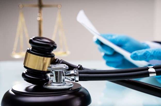 Medical malpractice. Person with medical glove holding stethoscope resting on gavel.