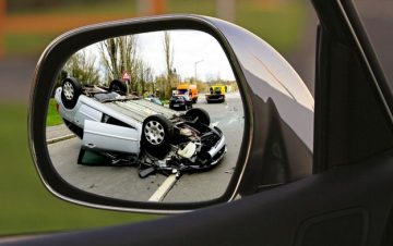 Car flipped over pictured in side mirror of another car. Avoid these mistakes that could hurt your car accident settlement.