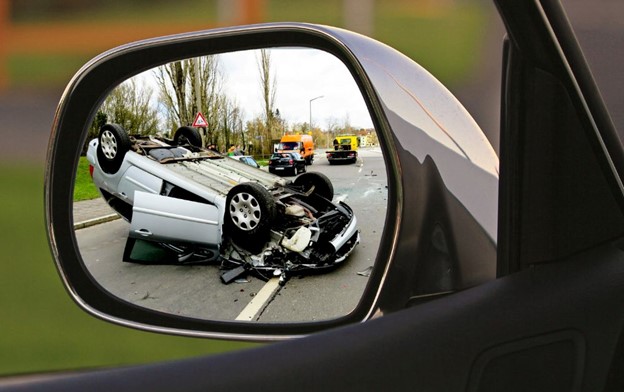 Car flipped over pictured in side mirror of another car. Avoid these mistakes that could hurt your car accident settlement.