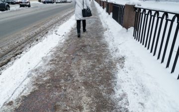 Person walking on snowy sidewalk. Avoid a sidewalk accident.