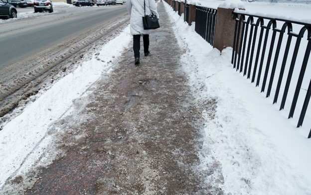 Person walking on snowy sidewalk. Avoid a sidewalk accident.